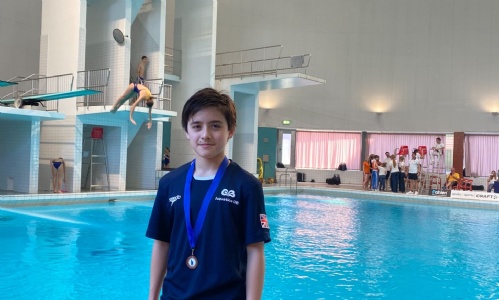 Josh posing in front of the swimming pool with his medal